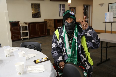 Person with mask, winter clothes, and high-vis jacket giving peace sign with fingers